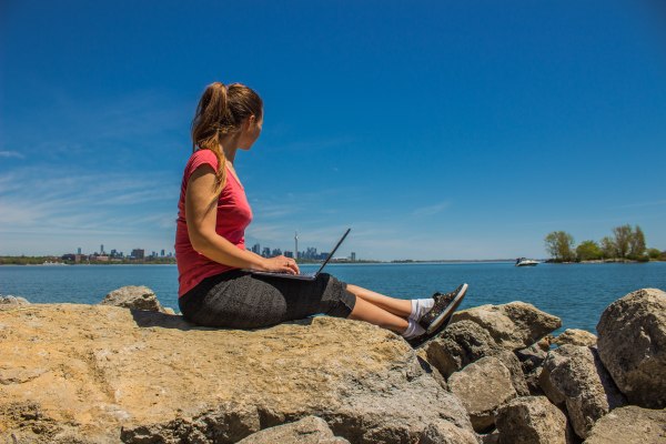 Joven mexicana con Working Holiday Visa que trabaja en su laptop mientras mira el skyline de Toronto, Canadá.