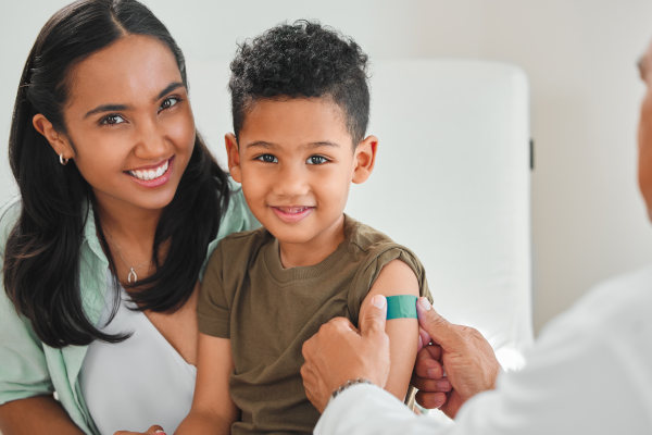 Doctor colocando venda en el brazo de un niño sonriente, acompañado por su madre, después de recibir una vacuna