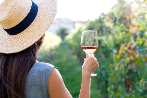 Mujer turista con sombrero sosteniendo copa de vino rosa durante una degustación en viñedo.