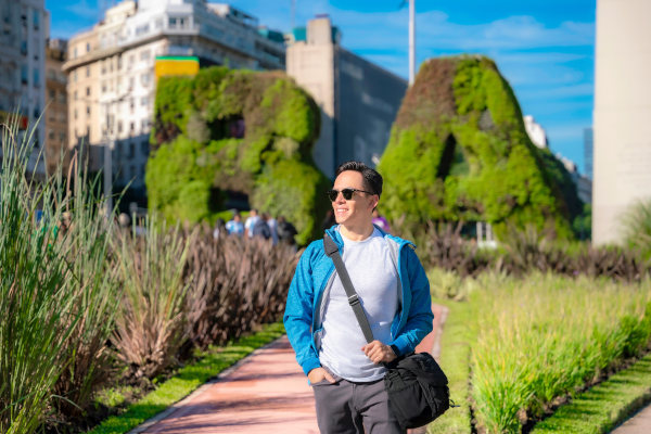 Hombre joven con lentes de sol caminando cerca de esculturas verdes con las letras “B”y “A”en Buenos Aires, Argentina