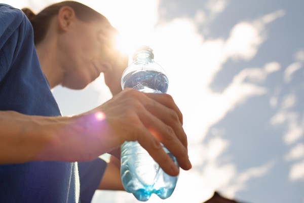 Primer plano de una botella de agua llena en la mano de una persona que sufre el calor debajo de un sol intenso.