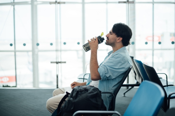 Hombre que bebe agua en un aeropuerto para prevenir el jet lag.