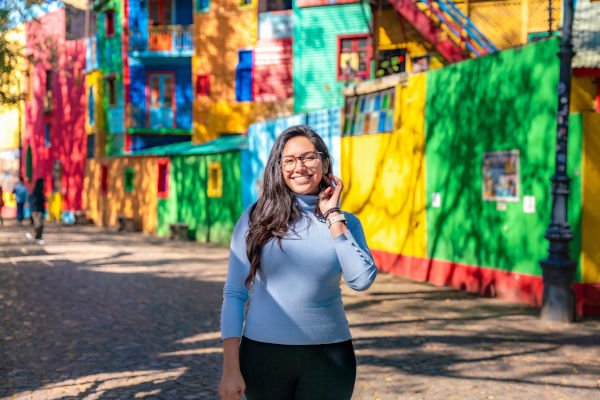 Joven turista sonriendo frente a las coloridas casas de Caminito, La Boca, Buenos Aires.