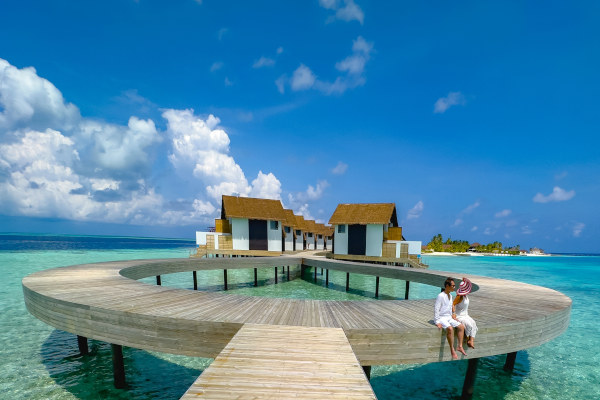 Pareja de blanco en un embarcadero de playa tropical cerca de la villa de agua en Maldivas.