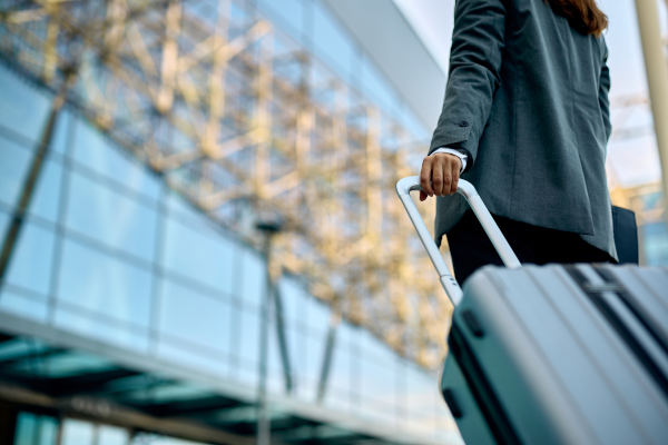 Vista de una mujer de negocios con maleta llegando a un aeropuerto irreconocible.