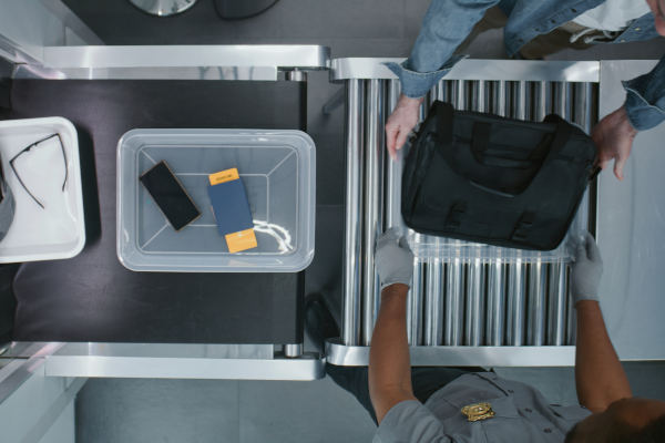 Vista superior de viajero colocando artículos personales en bandejas de plástico para la exploración de rayos X en la cinta transportadora.