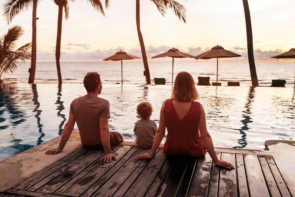 Familia sentada en el borde de una piscina con vistas a sombrillas y mar al atardecer.