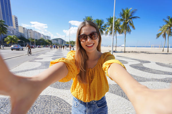 Mujer turista sonriente tomándose una selfie en el paseo de mosaicos ondulados blancos y negros de la playa de Copacabana en Río de Janeiro, Brasil.