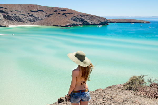 Mujer joven con sombrero de playa admirando la vista de Playa Balandra desde lo alto de un acantilado