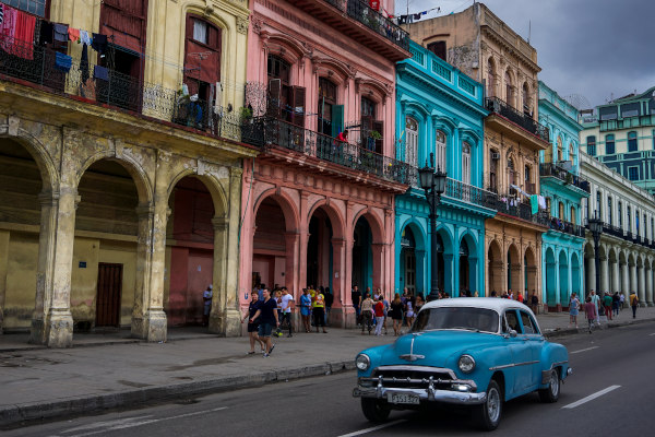 Auto antiguo clásico cubano por las calles de La Habana, con fachadas coloridas y peatones de fondo.