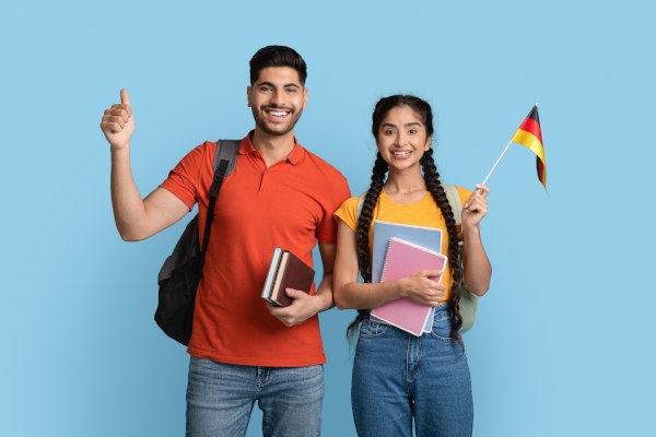 Estudiantes sonrientes con libros, mochilas y bandera alemana sobre un fondo celeste listo.