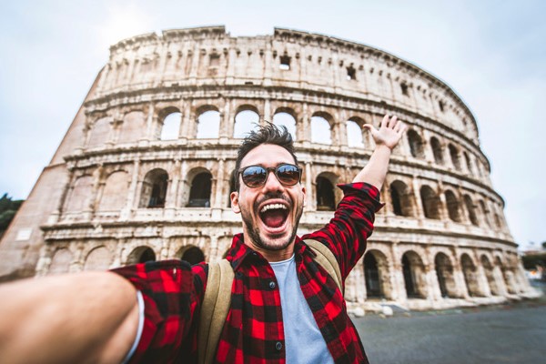 Chico sonriente tomándose selfie con el Coliseo romano de fondo