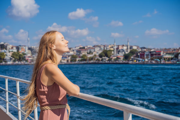 Mujer en la barandilla de un crucero por el Bósforo disfrutando de la brisa marina con los ojos cerrados en un día soleado.