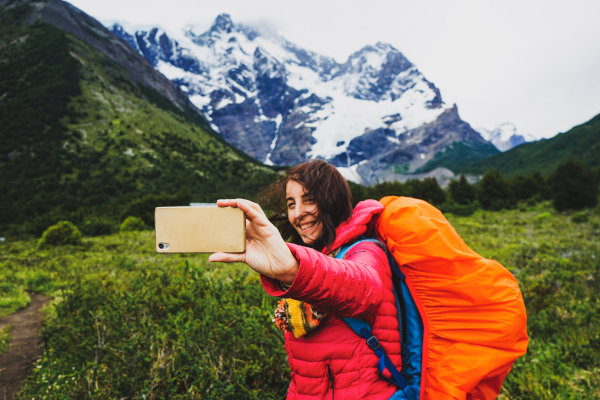 Turista con amplia mochila tomándose una selfie en un sendero cercano a una montaña nevada en la Patagonia chilena.