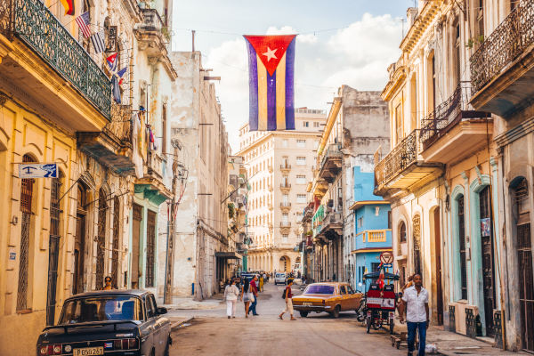 Bandera cubana colgada sobre una calle de La Habana, Cuba, con algunos autos y peatones en los alrededores.