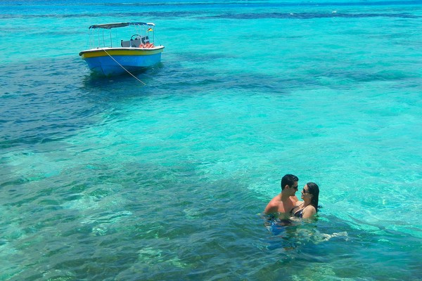 Pareja romántica en las aguas turquesas del Mar Caribe con un pequeño barco de fondo.