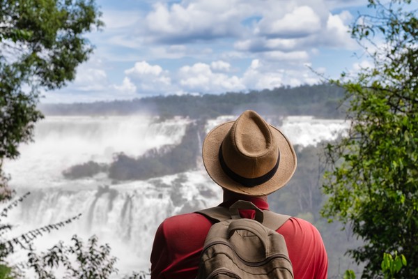 Hombre viajero con mochila y sombrero mirando las Cataratas del Iguazú en Paraná, Brasil.