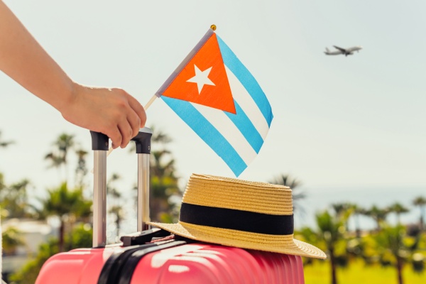 Persona viajando con maleta y pasaporte, sosteniendo un banderín de Cuba, en referencia a la eVisa para viajar al país.