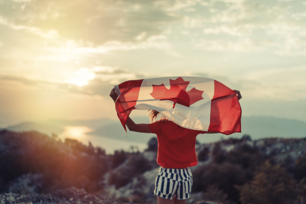 Niña ondeando la bandera de Canadá sobre sus hombros al atardecer.