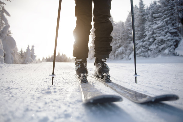 Vista de pies humanos en tablas de esquí y bastones de esquí en una pista nevada en un día soleado.