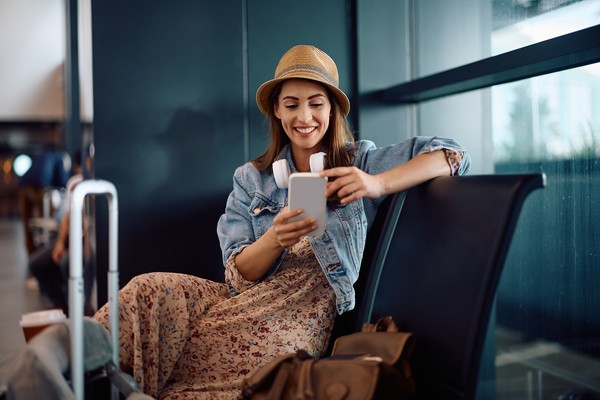 Mujer feliz usando smartphone mientras espera su vuelo en el aeropuerto.