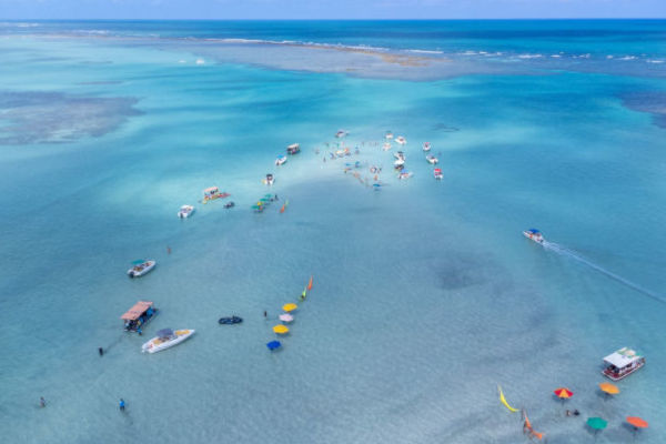 Vista aérea de las piscinas naturales de Maragogi, con embarcaciones y turistas disfrutando del mar.
