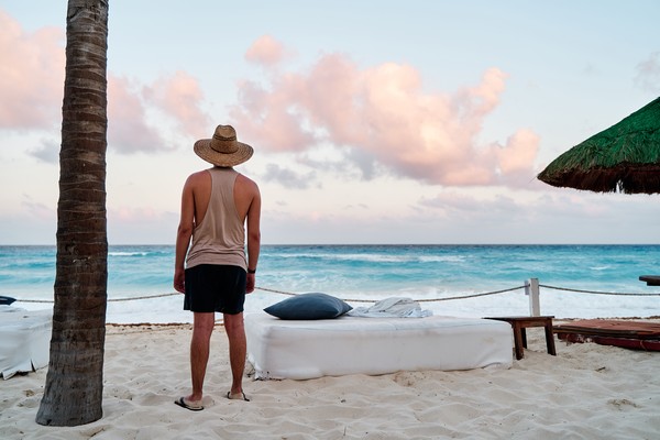 Hombre con sombrero en un club de playa mirando el mar turquesa de Cancún.