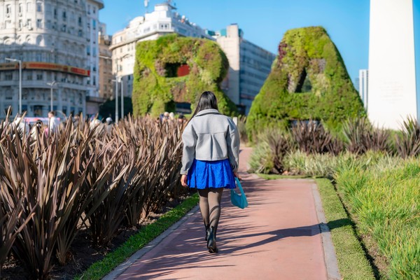 Mujer latinajoven con pelo largo caminando con confianza por las letras BA en Buenos Aires, Argentina