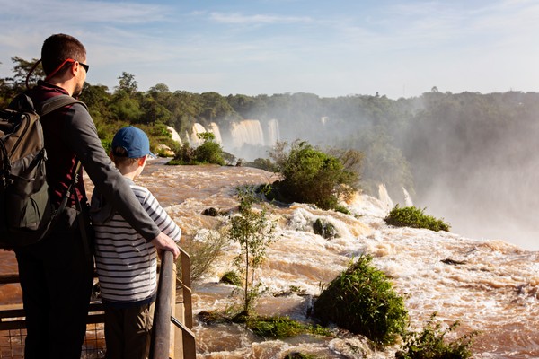 Padre e hijo contra una barandilla viendo las cataratas.