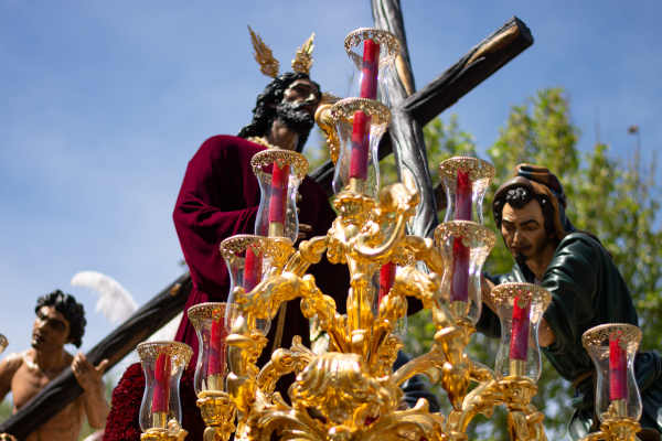 Imagen de Jesucristo cargando la cruz durante una procesión de Semana Santa, acompañado por fieles en una celebración religiosa.