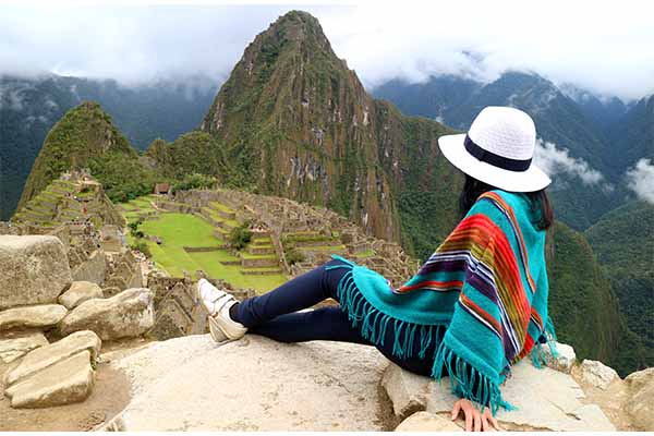 Mujer vestida con poncho observando las ruinas de Machu Picchu