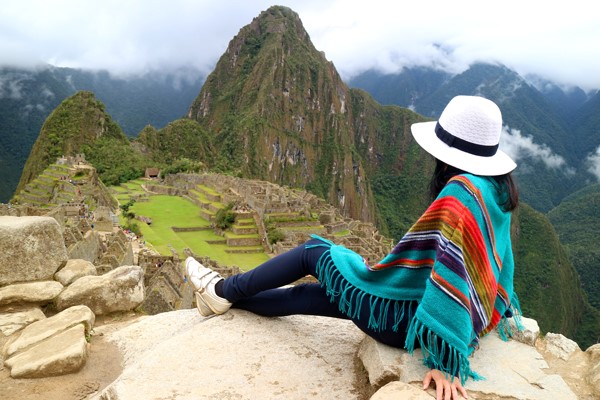 Mujer colombiana feliz planeando su viaje a Perú desde casa, con maleta abierta, pasaporte y laptop sobre la mesa.