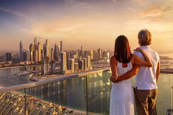 Mujer colombiana feliz planeando su viaje a Emiratos Árabes Unidos desde casa, con maleta abierta, pasaporte y laptop.