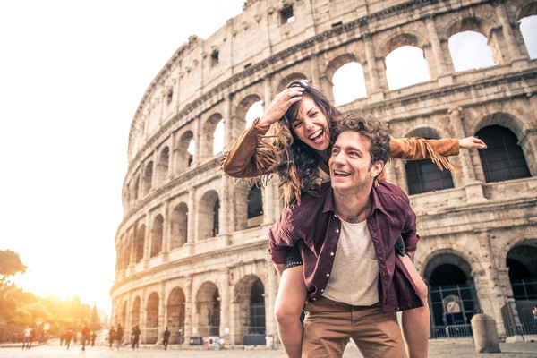 Pareja feliz con el Coliseo Romano de fondo al atardecer.