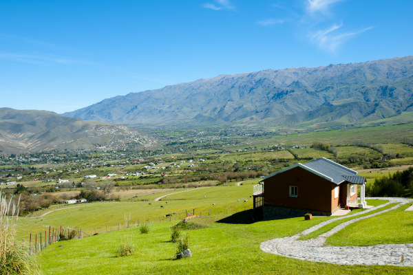 Vista de Tafí del Valle, Tucumán, Argentina, en un día soleado. Casa en medio de un prado con sierras y el resto del pueblo de fondo.