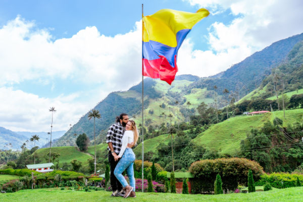 Pareja abrazada junto a una bandera de Colombia en un paisaje montañoso del Valle del Cocora.